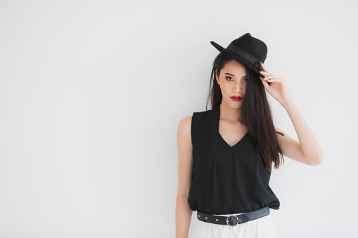 Sexy Asian model woman in black shirt and white pants, wearing hat, standing and posing, studio shot on white background.