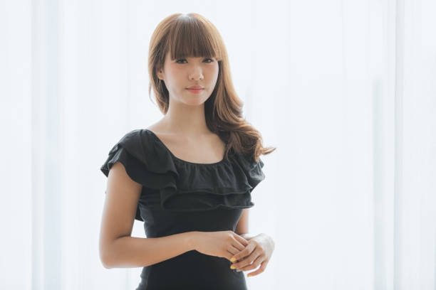 Shot of happy young beautiful Asian woman with brace retainers, curly long brown hair in black dress standing arms crossed and smiling to camera on isolated white background