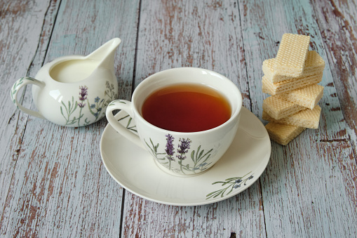 Top view of a mug with red tea, wafer biscuits and milk on wooden table