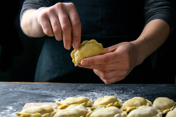 istock Cook in a dark jacket prepares dumplings. over a dark table on which the finished dumplings are laid out. Front views, close-up 1223600225
