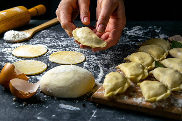 istock Cook in a dark jacket prepares dumplings. over a dark table on which the finished dumplings are laid out. Front views, close-up 1223600236