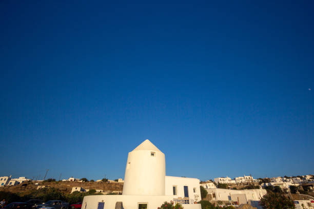Parikia, Paros, GR - 22 August 2025: A traditional windmill stands next to blooming bougainvillea with the Aegean Sea in the background