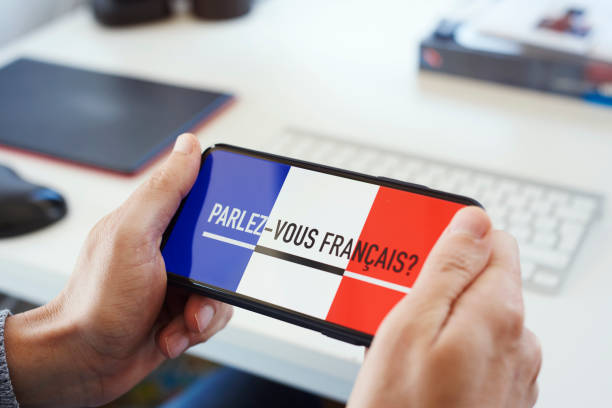text do you speak French in French in a smartphone closeup of a young caucasian man, sitting at a desk, having his smartphone in his hands with the text do you speak French written in French in its screen french language photos stock pictures, royalty-free photos & images