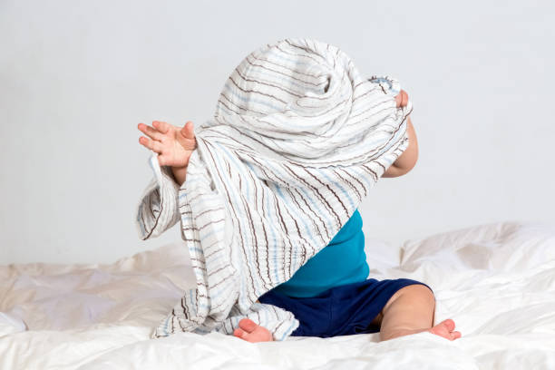 Caucasian Toddler playing under a striped blanket on white duvet bedding