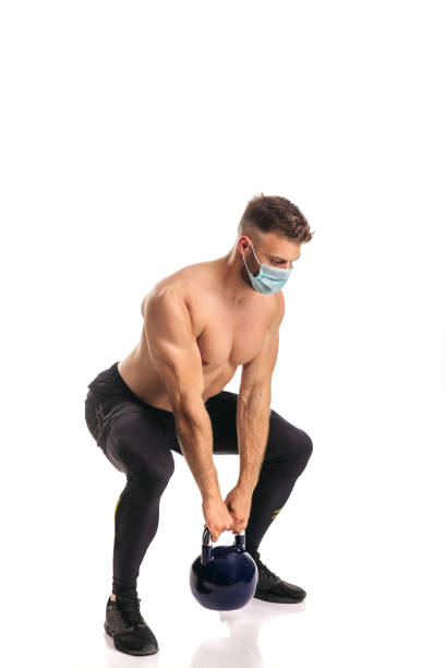 istock Young muscular male working out in studio with mask on his face 1223611473