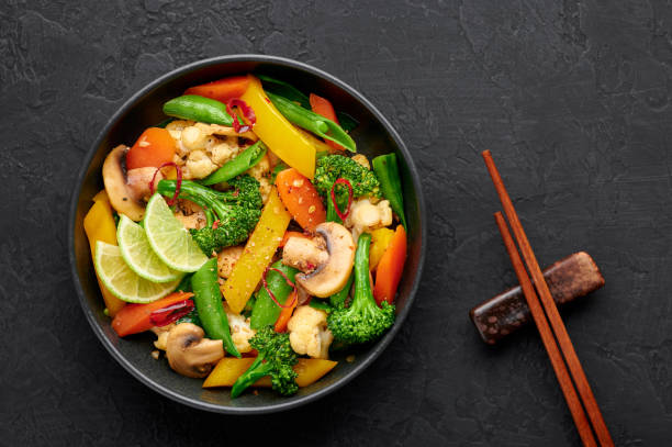 パッドパクルアムまたは野菜タイ炒め野菜は、暗いスレートを背景に黒いボウルで。pad pakはタイ料理のベジタリアン料理で、野菜とソースを混ぜ合わせた料理です。タイ料理。トップビュー - thai cuisine wok food thai culture ストックフォトと画像