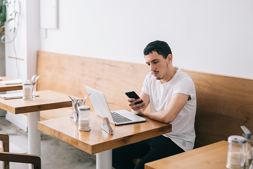 Young man sitting in a cafe and working and checking messaged from smartphone.