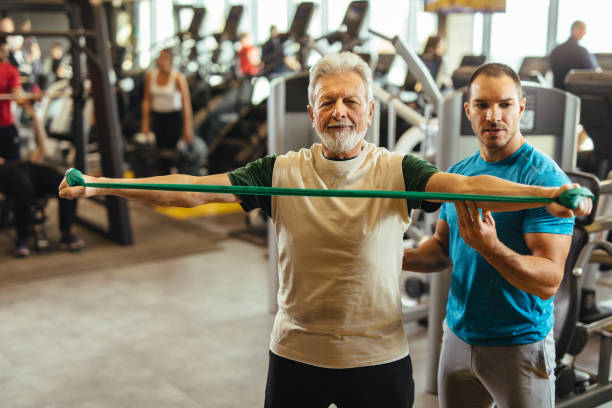 istock Male instructor assisting senior man exercising with resistance band at gym 1223618721