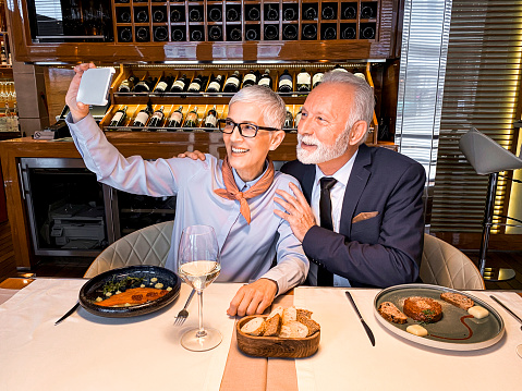 Two seniorpreneurs taking a selfie on a smart phone during a meeting in a cozy restaurant.