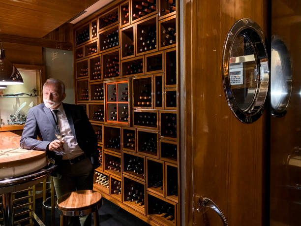 와이너리 지하실에서 화이트 스파클링 와인을 구불구이하면서 나침반이있는 나무 테이블에 앉아있는 수석 와인 테이스터 - winetasting wine wine rack bar counter 뉴스 사진 이미지