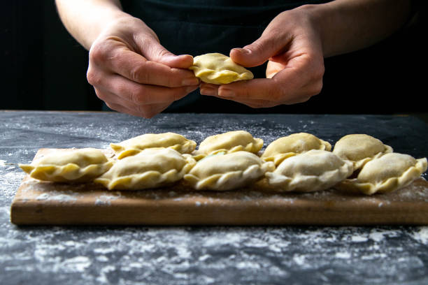 istock Cook in a dark jacket prepares dumplings. over a dark table on which the finished dumplings are laid out. Front views, close-up 1223627745