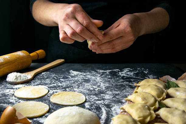 istock Cook in a dark jacket prepares dumplings. over a dark table on which the finished dumplings are laid out. Front views, close-up 1223627782