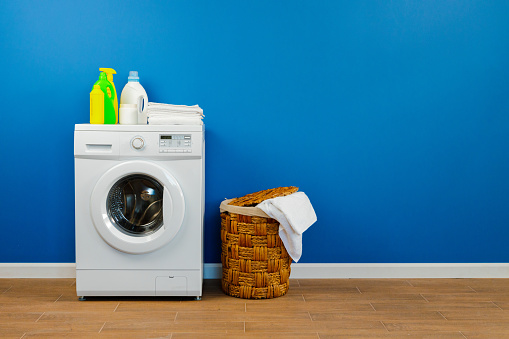 Washing machine with laundry on blue wall background, close up.