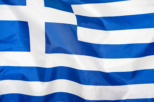 Fabric texture flag of Greece. Flag of Greece waving in the wind. Greece flag is depicted on a sports cloth fabric with many folds. Sport team banner.