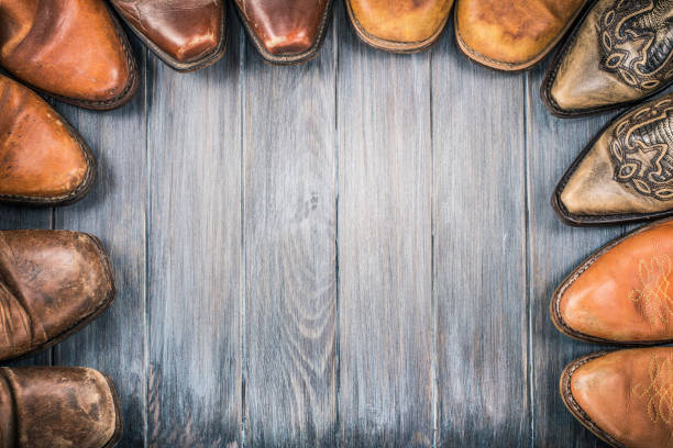 viejas botas de vaquero de cuero retro sobre suelo de madera texturizado envejecido para fondo. concepto nostálgico del salvaje oeste. foto filtrada estilo vintage - wanted poster fotos fotografías e imágenes de stock