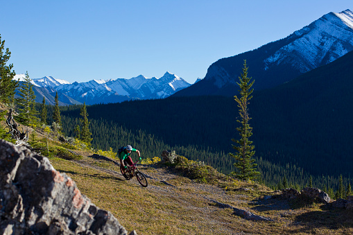 A man goes for a mountain bike ride in the Rocky Mountains of Canada. He is riding a modern enduro-style mountain bike, wears a cycling helmet and a smart watch.