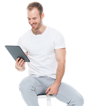 One person of aged 30-39 years old with with beard caucasian young male in front of white background wearing pants who is showing cool attitude and using touch screen