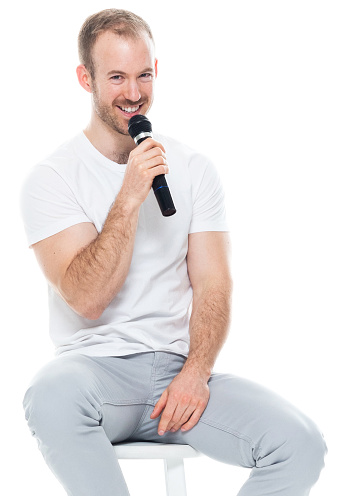 Waist up of aged 30-39 years old with with beard caucasian young male in front of white background wearing pants who is showing cool attitude and holding microphone