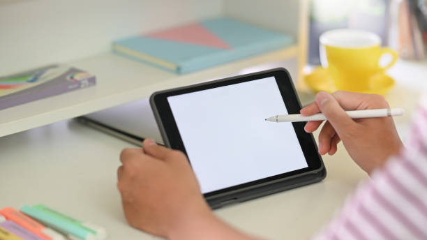istock Cropped image of creative people hands' holding a cropped black computer tablet with white blank screen and stylus pen while sitting at the modern white working desk over comfort room as background. 1223655158