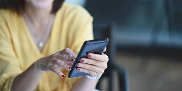istock Cropped image of woman's hands using/holding a smartphone while sitting and relaxing over comfortable living room as background. 1223655201
