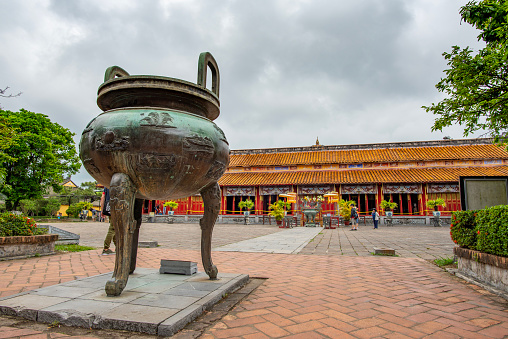 Hue, Vietnam - April 15, 2018: One of the famous urn (caldron) of the Hue citadel with very few tourists and an overcast sky
