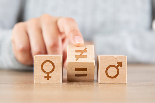 Female hand turns a dice and changes unequal sign to equal sign between symbols of men and women
