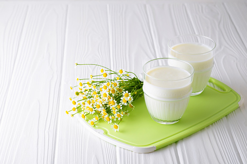 Homemade fermented dairy product kefir or yogurt with probiotics in glasses on a white wooden background with flowers with copy space.Horizontal orientation. Kefir Lose weight diet concept.