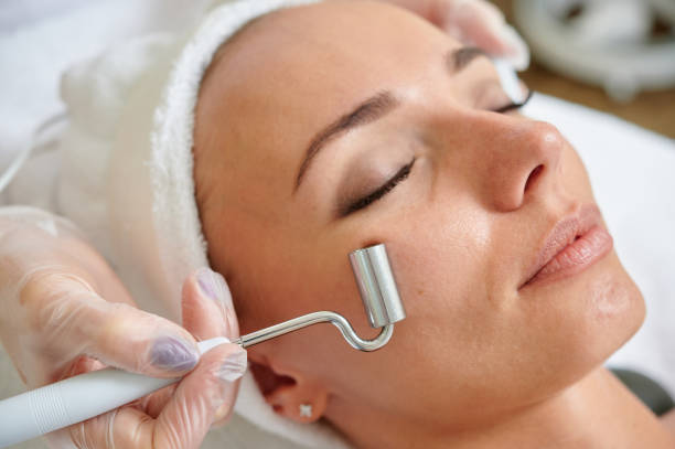 Female receiving electric facial treatment by cosmetologist wearing gloves professional services. stock photo