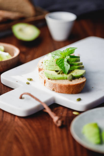 istock Avocado toast with pepitas and fresh basil on a white marble cutting board. Home cooking, healthy eating concept. 1223671965
