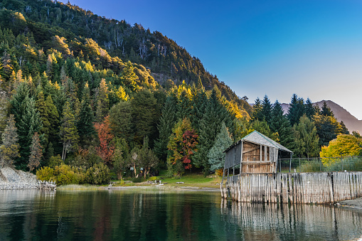 small cabin on a beautiful lake surrounded by multicolored trees in autumn