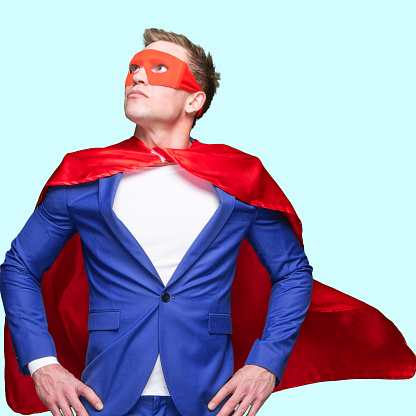 Front view of with brown hair caucasian young male hero standing in front of colored background wearing costume who is in concentration with hand on hip