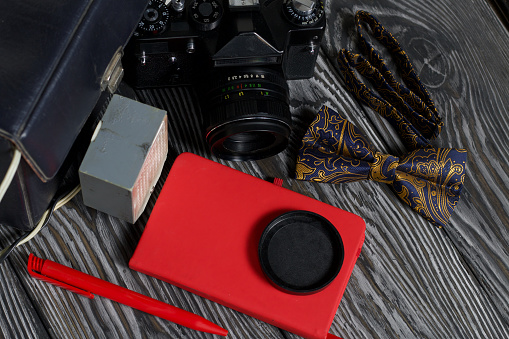Photographer accessories. Camera, flash, bow-tie, notebook and pen. On brushed pine boards.
