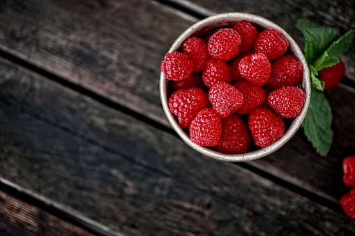 This is a overhead photo of fresh raspberries in a handmade ceramic bowl on an old wood table.