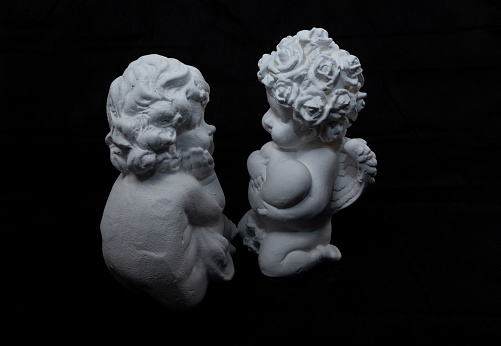 two white figures of angels on a dark background seem to be talking to each other. molded from plaster or ceramics