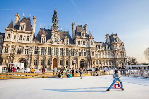 People skate on the ice rink in front of the City Hall building in downtown Paris France on a sunny day.