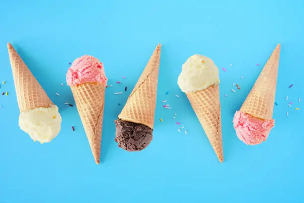 Photo of Ice cream cone flat lay over a blue background with vanilla, strawberry and chocolate flavors