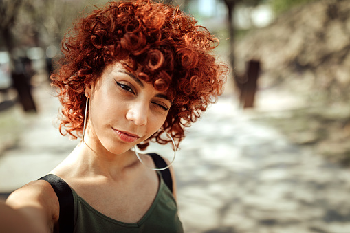 Young redhead Latin woman smiling and taking selfie outdoor