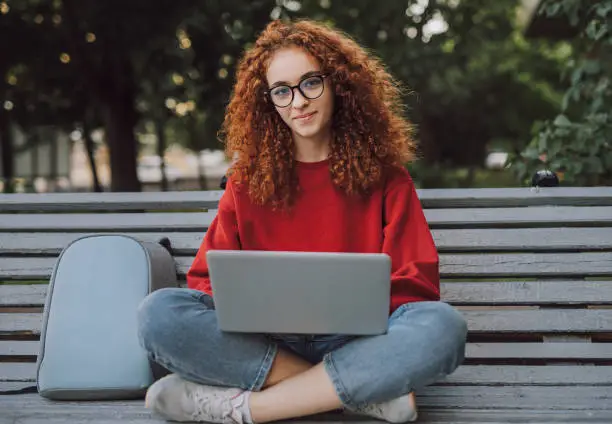 Photo of Positive young woman with laptop sitting on bench in city