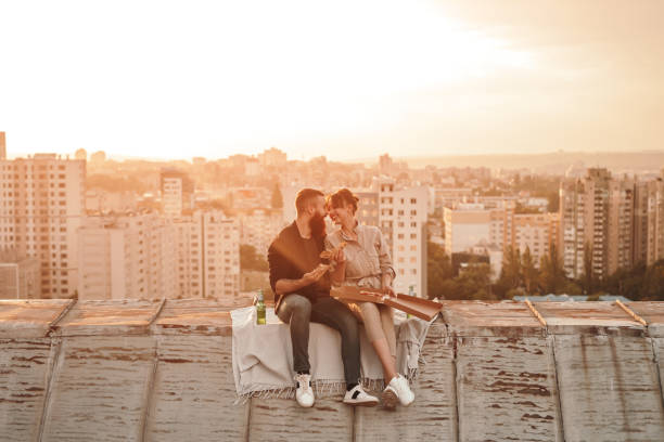 glückliches junges paar essen pizza auf dem dach - freunde imbiss großstadt stock-fotos und bilder
