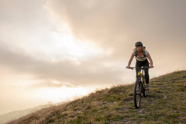 Photo of Young woman rides up grassy hillside on electric mountain bike
