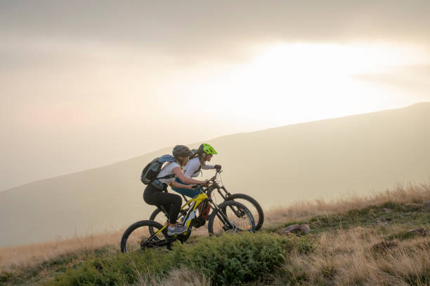 istock Two women ride up grassy hillside on electric mountain bikes 1223716796