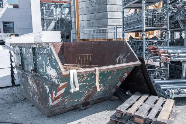 Photo of on a construction site, a waste container stands next to a shelf with scaffolding parts