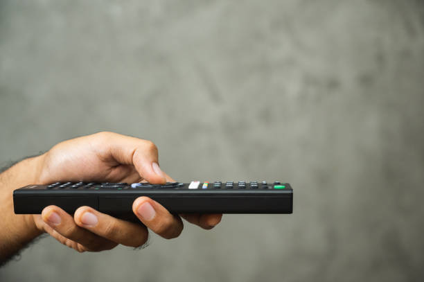 istock Young man holding television remote control. Hands pointing to tv set and turning it on or off select channel watching tv on his sofa at home in the living room relax. 1223732105