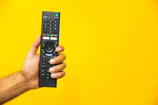 istock Close up male hand holding television remote control on isolated yellow background. 1223732182