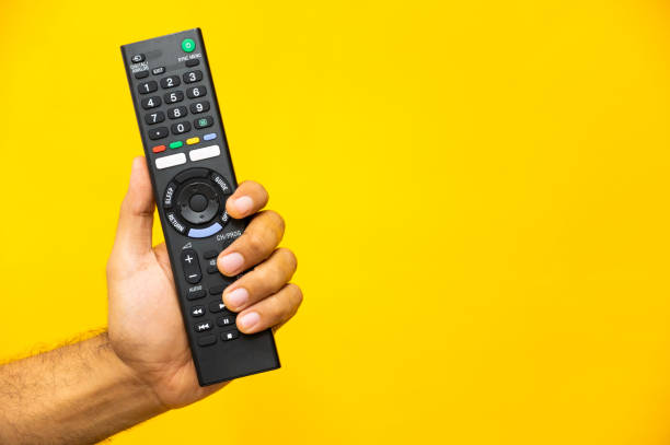 istock Close up male hand holding television remote control on isolated yellow background. 1223732256