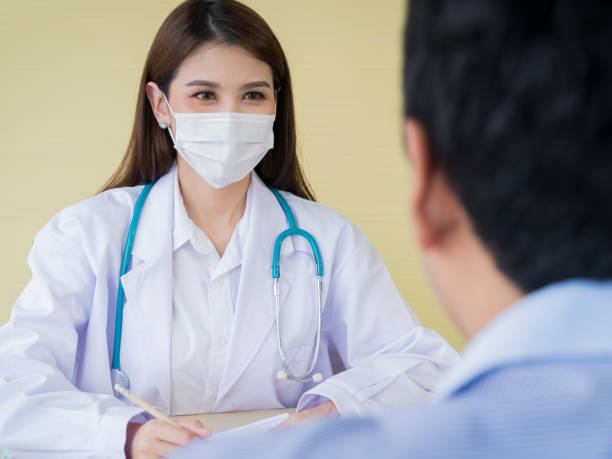 A female doctor is smiling face under the surgical mask and looking to male patients. stock photo