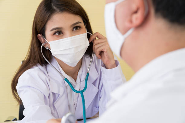 The female doctor wearing a surgical mask and using a stethoscope to check the pulse and look at a male patient, stock photo