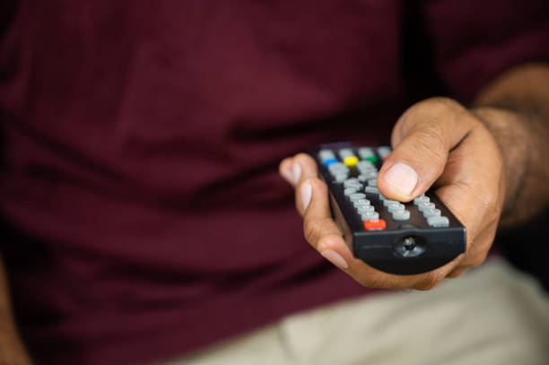istock Young man holding television remote control. Hands pointing to tv set and turning it on or off select channel watching tv on his sofa at home in the living room relax. 1223732942