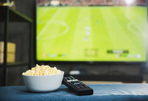 Photo of Popcorn and television remote control on football program tv screen background. Watching tv relax concept.