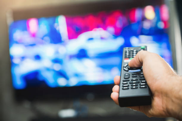 istock Young man holding television remote control. Hands pointing to tv screen set and turning it on or off select channel watching tv on his sofa at home in the living room relax. 1223733012